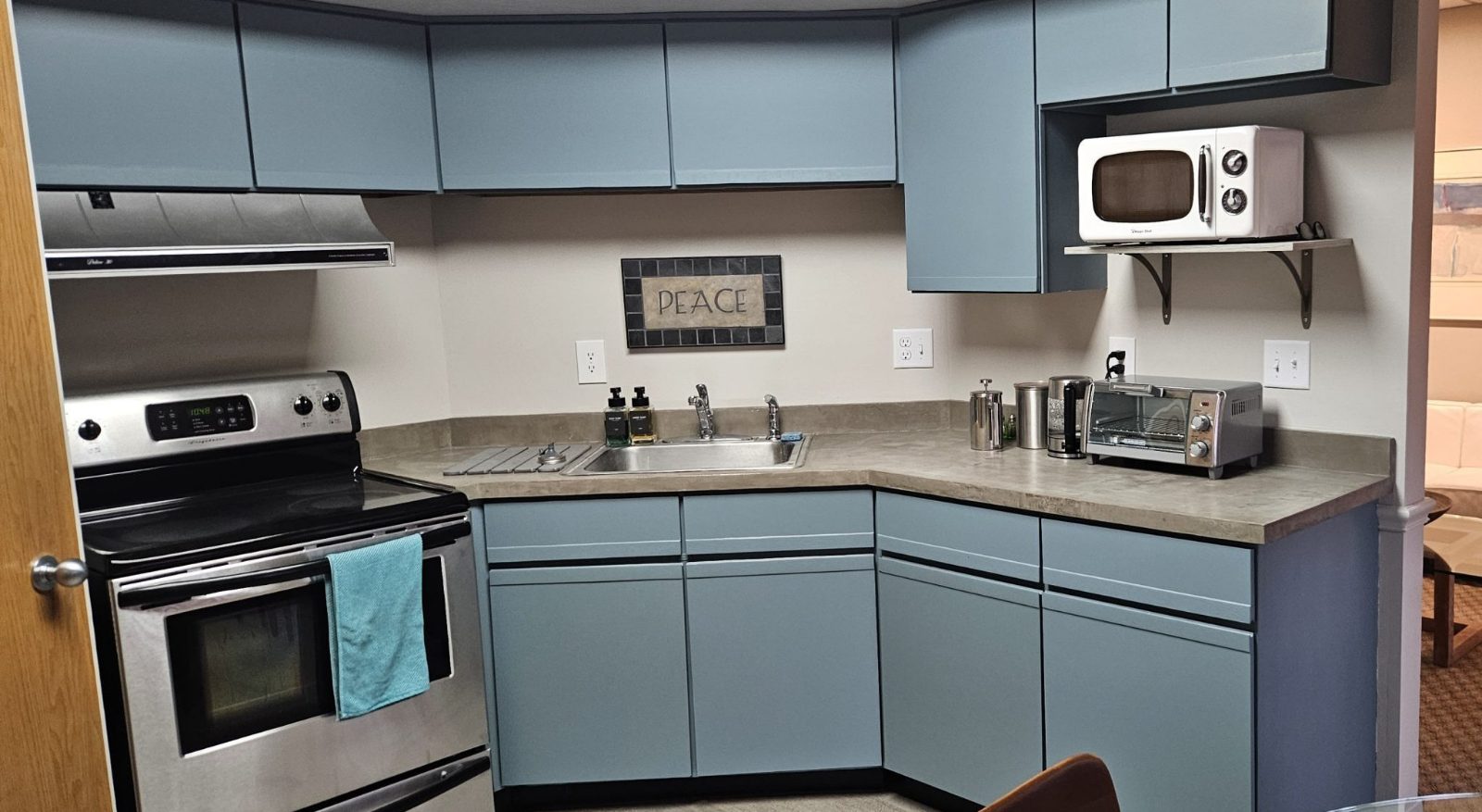 The kitchen: blue cabinets, an electric stove, a microwave and a toaster oven, with a small Peace sign on the wall
