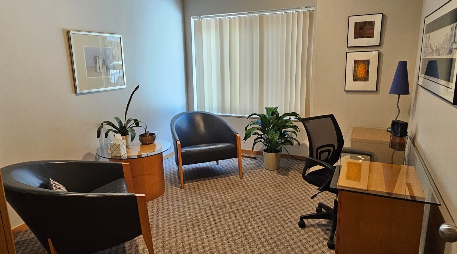The Grove: two dark leather armchairs, a round side table with a plant and a glass-topped desk beside a large window