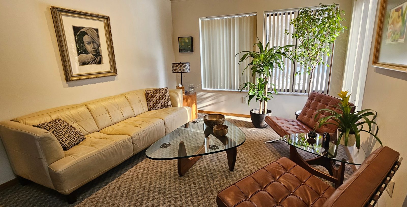 The Harbor: a cream leather sofa, glass coffee table and two brown leather lounge chairs beside tall windows and plants