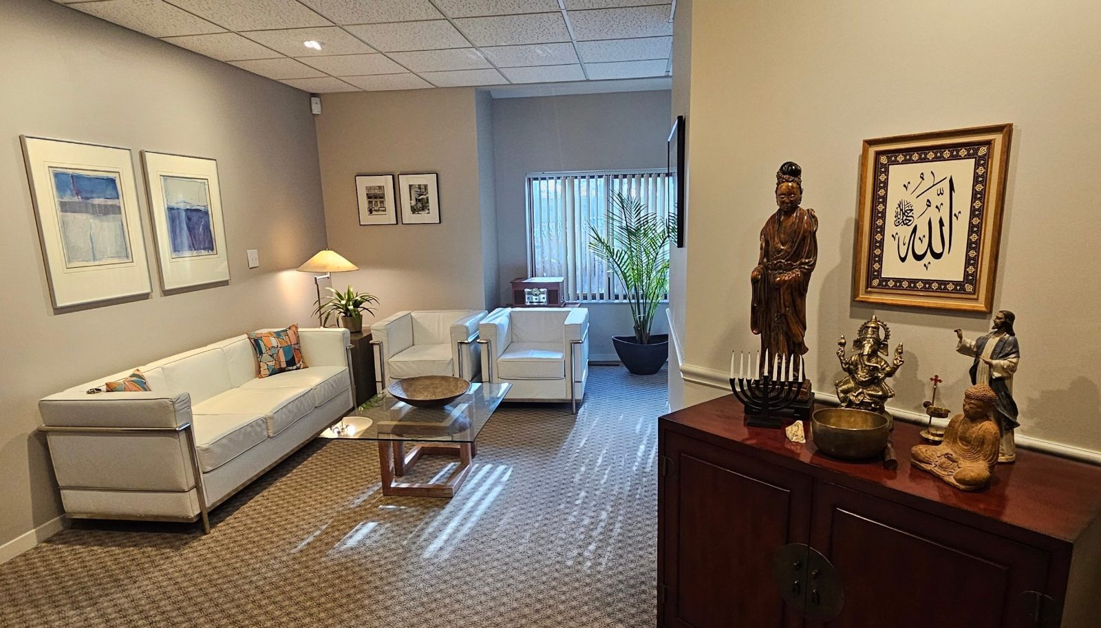 The waiting room: a white sofa and two white armchairs around a glass coffee table, with framed art on the walls
